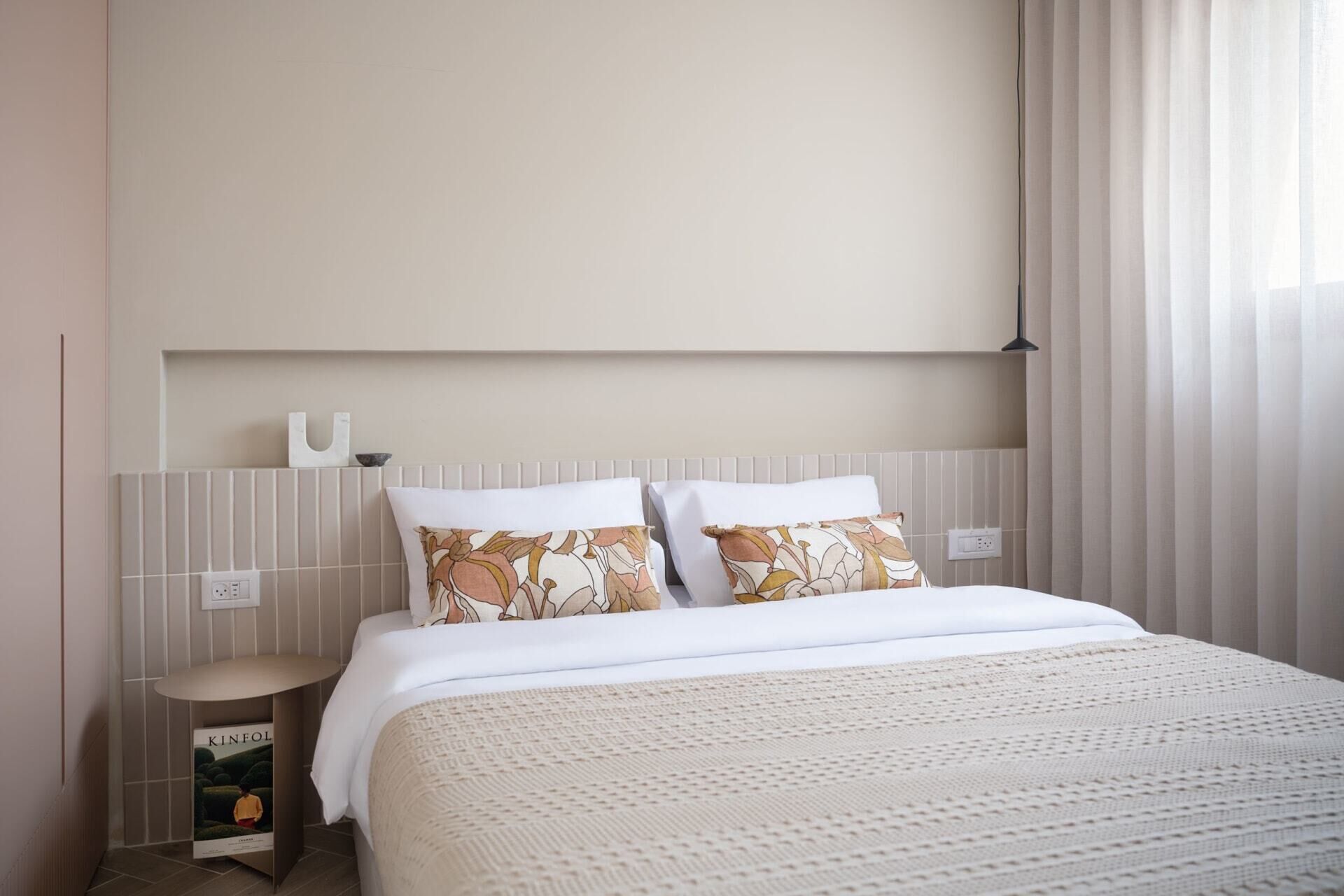 A neatly arranged hotel room with a bed, a nightstand, and a wall-mounted shelf.