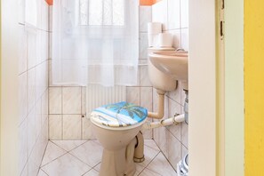 Et badeværelse med toilet, håndvask og et vindue med gardin.