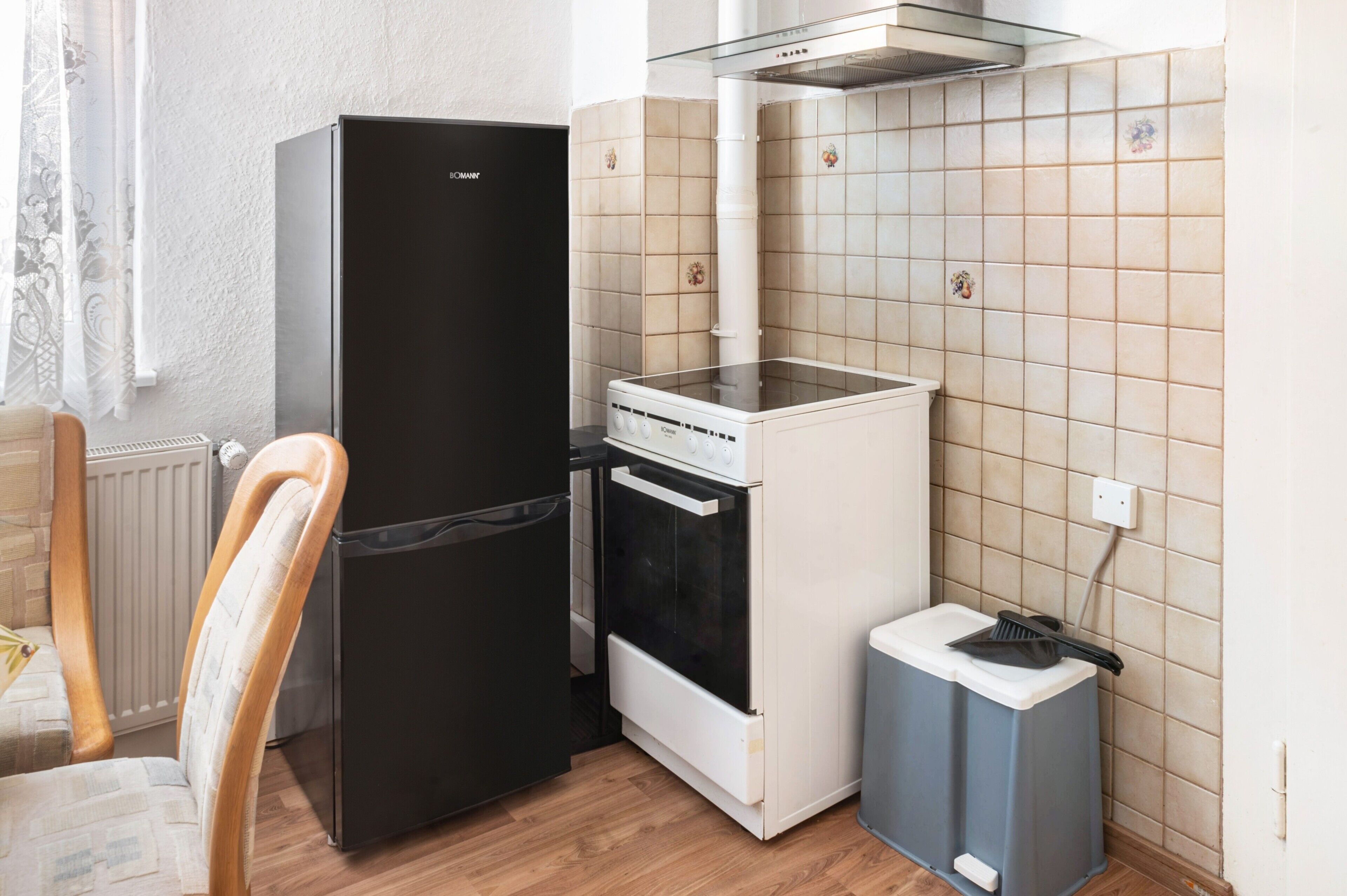 Eine kleine Küche mit einem schwarzen Kühlschrank, einem weißen Backofen und einer blauen Mülltonne.