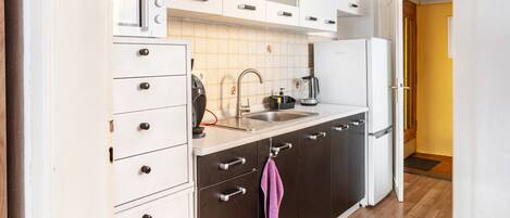 A kitchen with white cabinets, a stainless steel sink, a coffee maker, and a refrigerator.