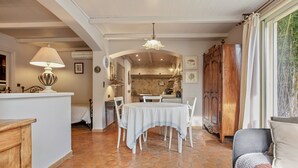Uma área de refeições com mesa e cadeiras, uma cozinha ao fundo e um armário de madeira.