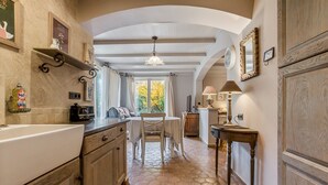 Uma cozinha com piso de azulejos, armários de madeira, mesa de jantar com cadeiras e uma janela com cortinas.