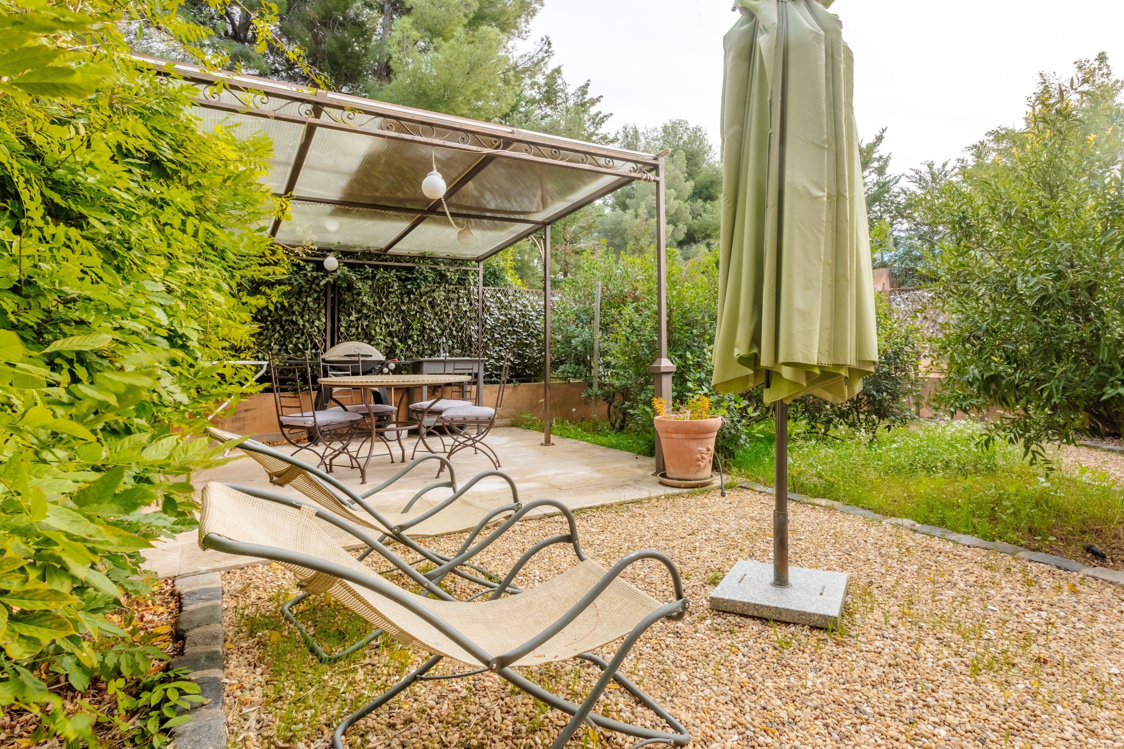 Un patio couvert aménagé avec du mobilier d’extérieur, un barbecue et une pergola agrémentée d’un luminaire suspendu.