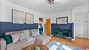 Un soggiorno con un divano angolare beige, un tavolino rotondo con piante, un tappeto azzurro decorato e una poltrona verde.