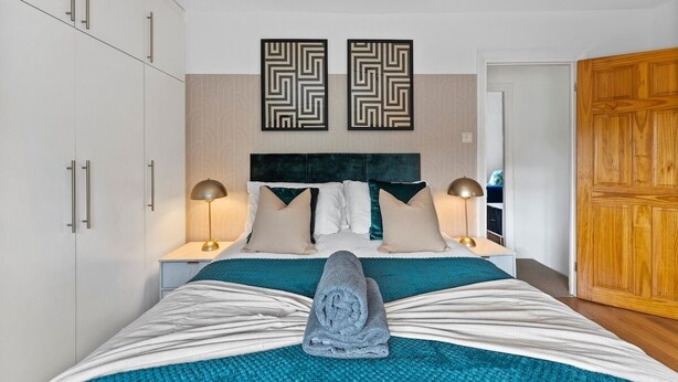 Un letto rifatto con cura, un asciugamano arrotolato, due pannelli decorativi a parete, lampade sui comodini e un armadio in legno.