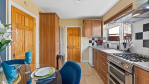 Una cucina funzionale con mobili in legno, un piano cottura a gas e una zona pranzo con tavolo in vetro e sedie blu.