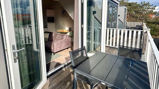 A modern outdoor deck with a glass door leading to a living area with a sofa and a table. - Lodge Located on the Church Square (Zoutelande)