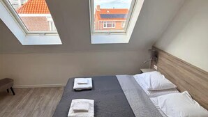 A room with a bed, two skylights, and a view of buildings. - Lodge Located on the Church Square (Zoutelande)