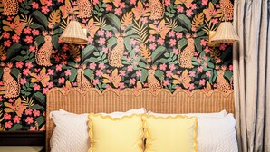 Ein Bett mit weißen und gelben Kissen, einem Weidenkopfzier und einer Wand mit tropischem Blumenmuster.