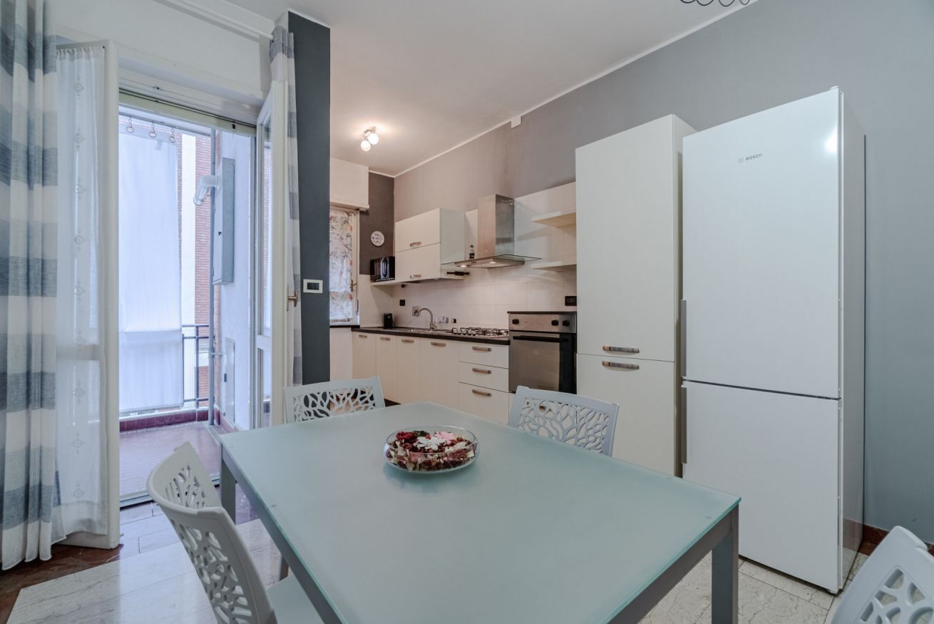 Une cuisine moderne avec des meubles blancs, un réfrigérateur blanc et une table à manger avec des chaises.