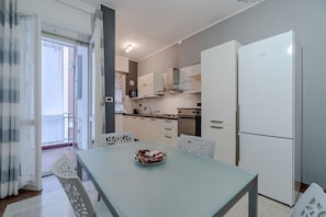Een moderne keuken met witte kasten, een witte koelkast en een eettafel met stoelen.
