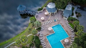 Vista aérea de un resort con piscina, sillas de descanso, sombrillas y un tobogán de agua.