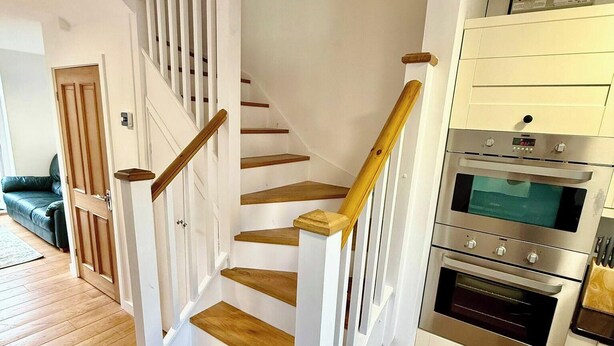 A staircase with wooden steps and white railings, leading to a kitchen area with a built-in oven and cabinets. - 2 Bed House - Sleeps 4 - Parking - Wifi (Cambridge)
