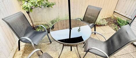 A patio with a round table and four chairs, a black umbrella, and a wooden fence.