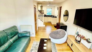 A modern living room with a green sofa, a coffee table, a round seating area, a TV, and a staircase leading to a kitchen. - 2 Bed House - Sleeps 4 - Parking - Wifi (Cambridge)