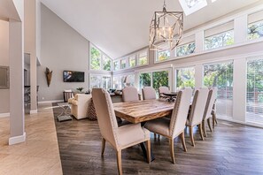 A spacious dining area with a large wooden table and multiple chairs, large windows, and a modern chandelier. - Elegant Sea Pines Getaway Near the Beach! (Hilton Head Island)