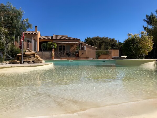 Una piscina cristalina con una casa al fondo.