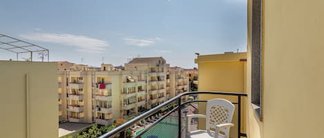 A balcony with a view of a residential building complex, a pool, and a chair.