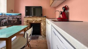 A compact kitchen with a stone fireplace, a flat-screen TV, and a red kettle. - Renovated studio in Lourdes - Rue de la Grotte, near the Sanctuary and the Pyrenees (Lourdes)