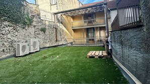 A two-story building with a stone facade, a balcony, and a fenced yard with artificial grass. - Renovated studio in Lourdes - Rue de la Grotte, near the Sanctuary and the Pyrenees (Lourdes)