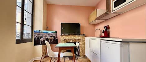 Une cuisine compacte comprenant un coin repas, un téléviseur et une fenêtre donnant sur un paysage où l’on peut voir des moutons.