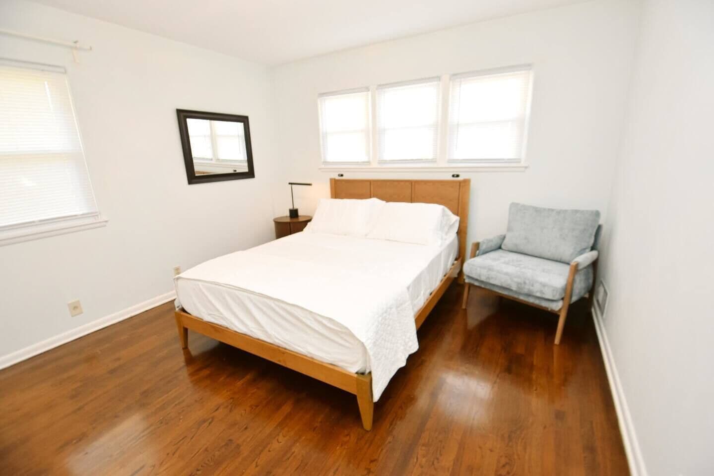 A bedroom with a wooden bed, a nightstand, a chair, and a framed picture on the wall.