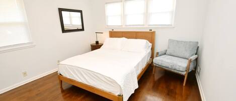 A bedroom with a wooden bed, a nightstand, a chair, and a framed picture on the wall.