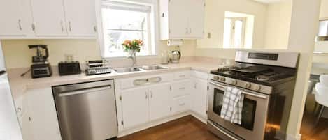 A modern kitchen with white cabinets, stainless steel appliances, and a wooden floor.