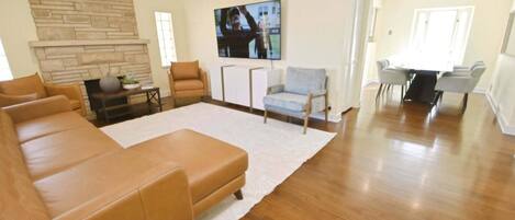 A spacious living room with a large leather sofa, a white rug, and a stone fireplace.