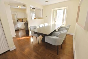 A dining area with a long table and six chairs, a kitchen in the background, and a window providing natural light. - Walkable to Notre Dame! Cozy 2 bedroom home(426) (South Bend)
