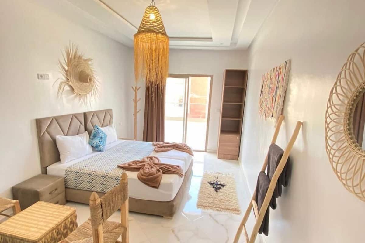 A modern bedroom with a bed, a hanging light fixture, a small table, and a chair.