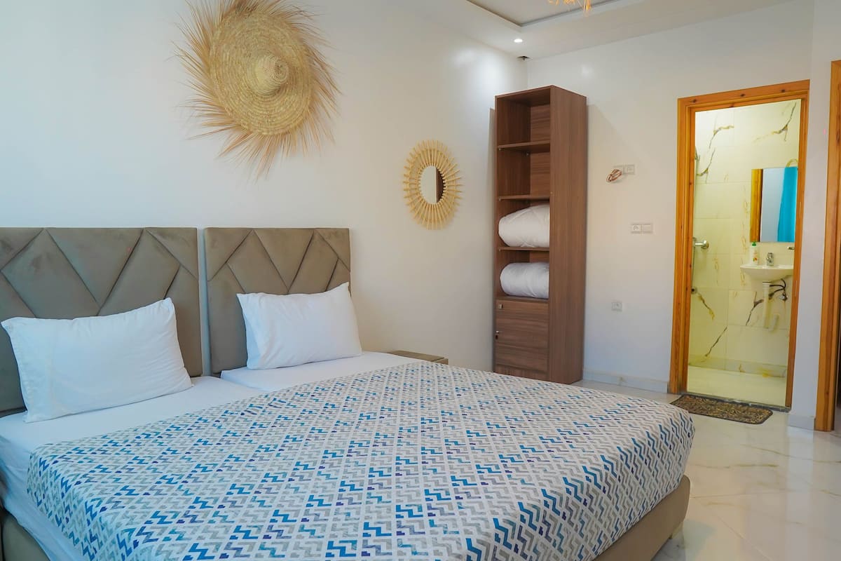 A bedroom with a bed, a wooden wardrobe, a mirror, and a door leading to a bathroom.