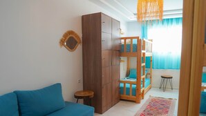 Ein Zimmer mit einem blauen Sofa, einem Kleiderschrank, einem Etagenbett, einem kleinen runden Tisch und einem gemusterten Teppich.