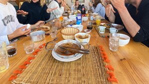 Eine Gruppe von Menschen speist an einem Holztisch mit einer gewebten Tischmatte, umgeben von verschiedenen Gerichten und Getränken.