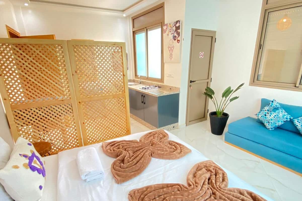A hotel room with a bed, a blue sofa, a desk with a sink, and a potted plant.
