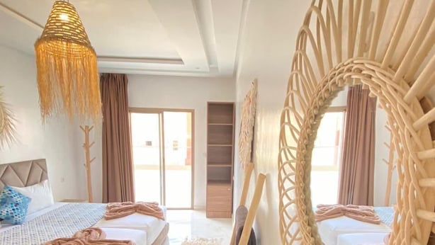 Ein modernes Schlafzimmer mit einem großen Bett, einer Hängeleuchte, einem dekorativen Spiegel und Blick ins Freie.