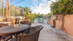 Une terrasse dotée de meubles en osier, d’un barbecue et offrant une vue sur une piscine.