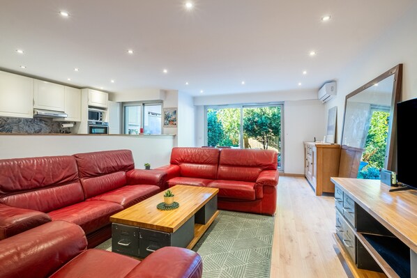 A modern living room with red leather sofas, a wooden coffee table, and a kitchen area with white cabinets and a microwave.