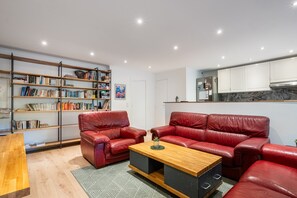 A modern living room with red leather sofas, a wooden coffee table, and a bookshelf filled with books.