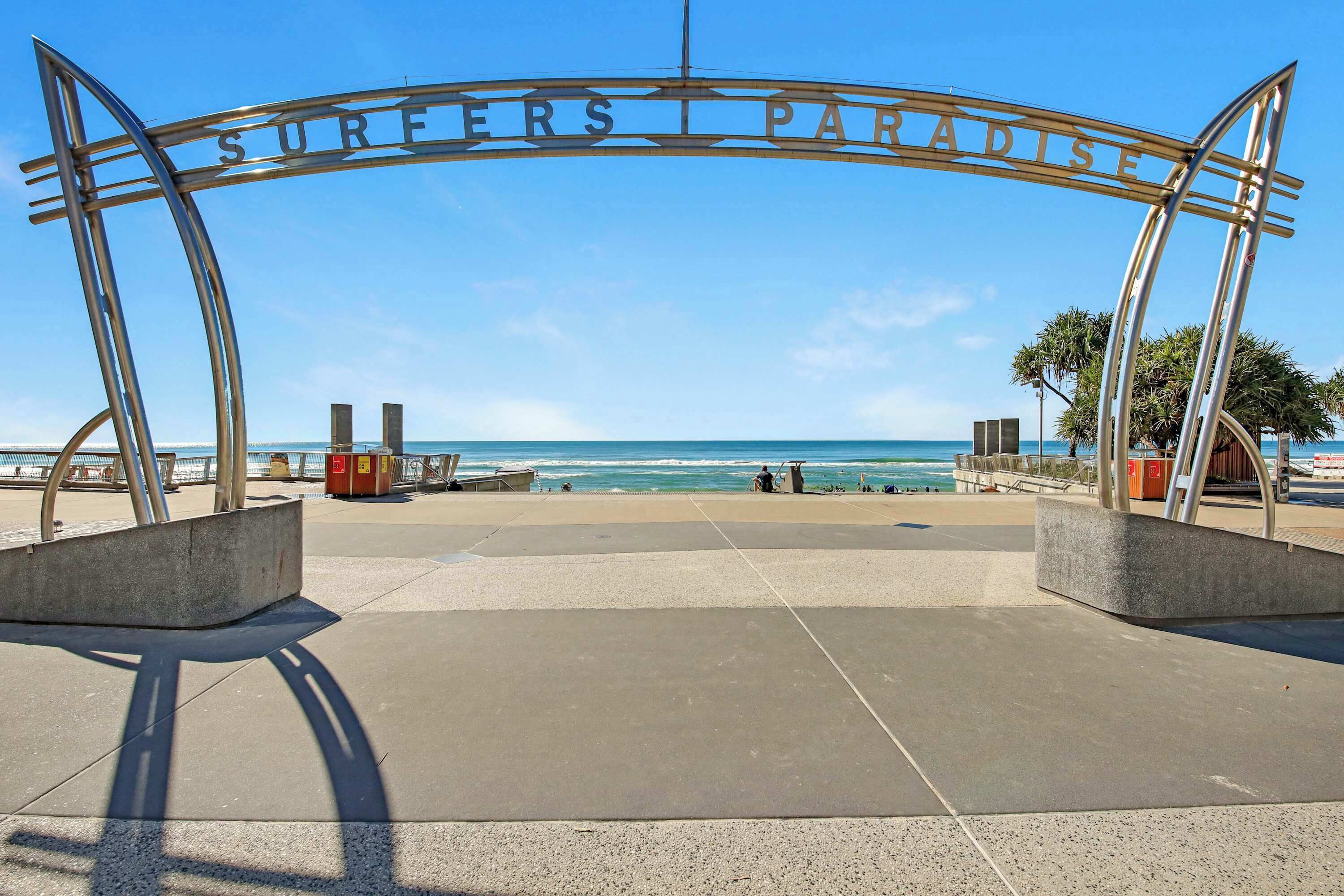 Una entrada a la playa con un cartel que dice "SURFERS PARADISE" y vista al océano.