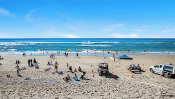 A beach with people sunbathing, a lifeguard vehicle, and a clear blue sky.
