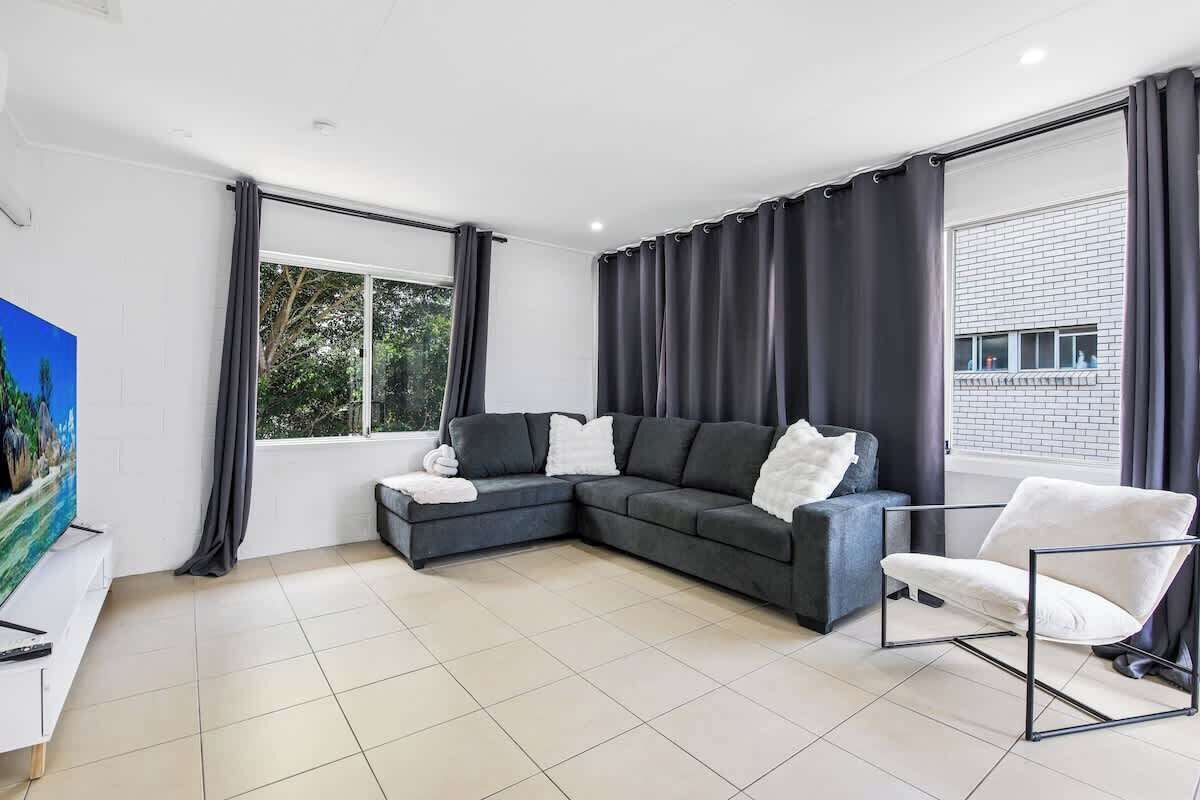 A modern living room with a sectional sofa, a white armchair, and a large window with curtains.