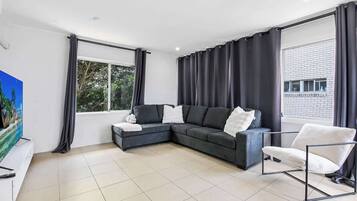 A modern living room with a sectional sofa, a white armchair, and a large window with curtains.