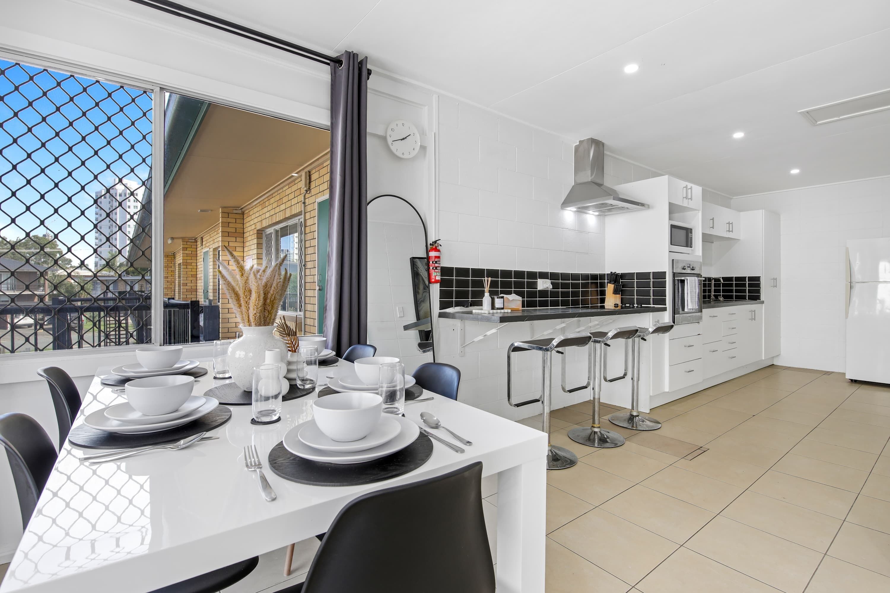 A modern kitchen with white cabinets, a black countertop, and a dining area with a white table set for four.