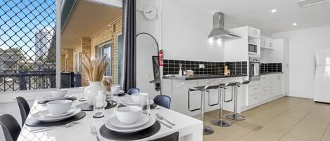 A modern kitchen with white cabinets, a black countertop, and a dining area with a white table set for four.