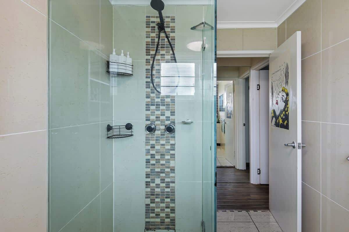 A glass-enclosed shower with a tiled wall, a showerhead, and a handrail.