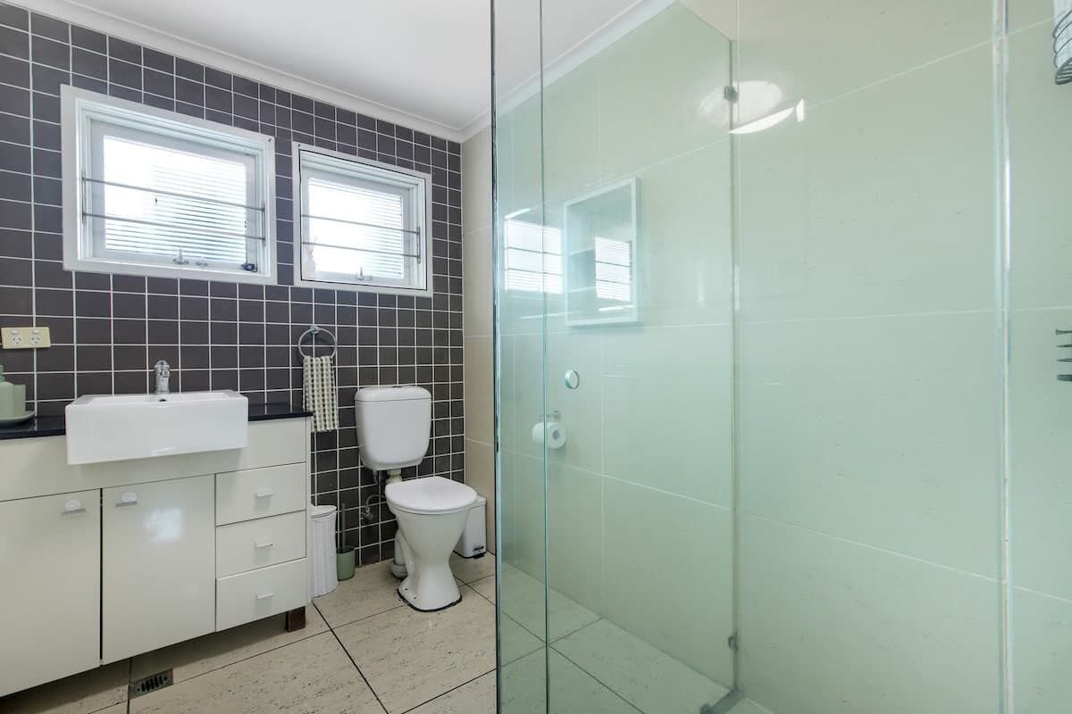 A bathroom with a white sink, two windows, a toilet, and a glass shower enclosure.
