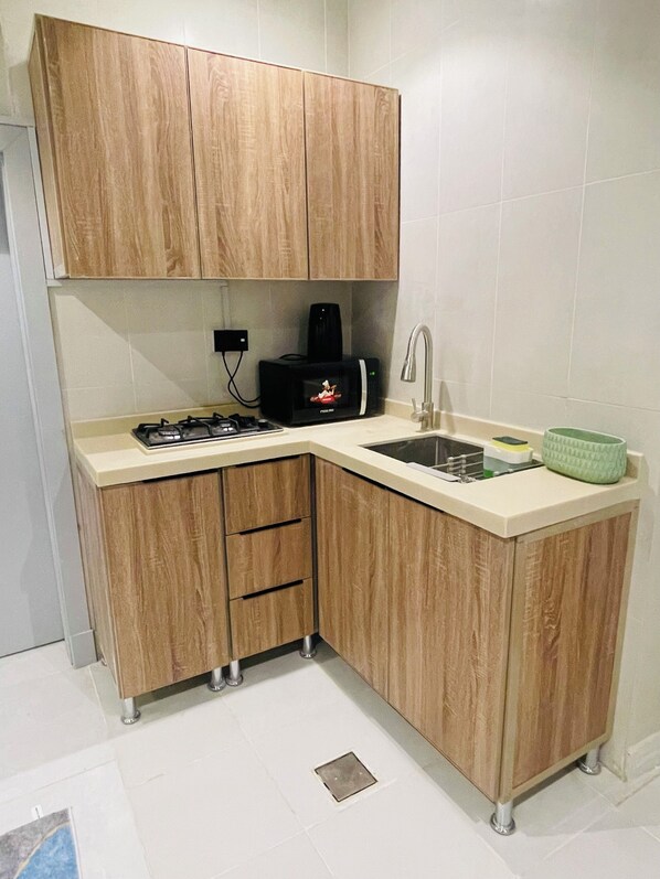 Een kleine keuken met houten kastjes, een ingebouwde magnetron, een gasfornuis en een spoelbak.