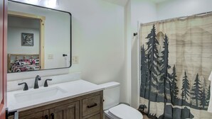 Um banheiro com pia branca, espelho e cortina de chuveiro com desenho de floresta.
