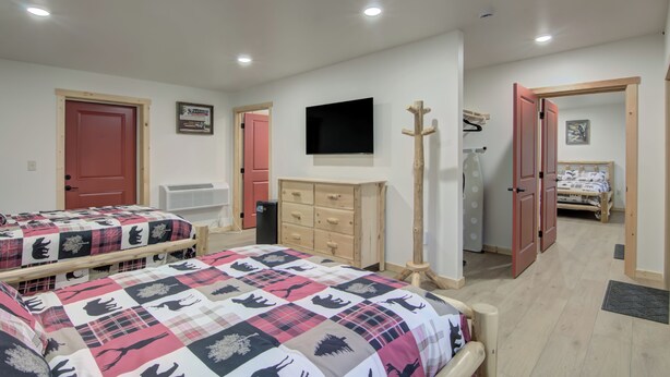 Quarto com duas camas, cômoda, televisão e porta para outro espaço.